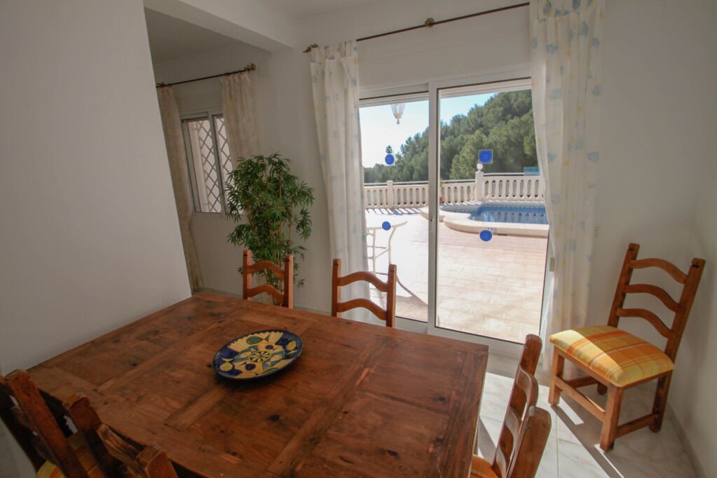 A wooden dining table with chairs, a potted plant, and a view of an outdoor pool and deck through a glass door.
