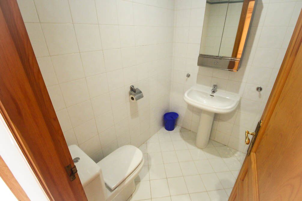 Ein kleines, sauberes Badezimmer mit weißen Fliesen, Toilette, Waschbecken und Spiegel.