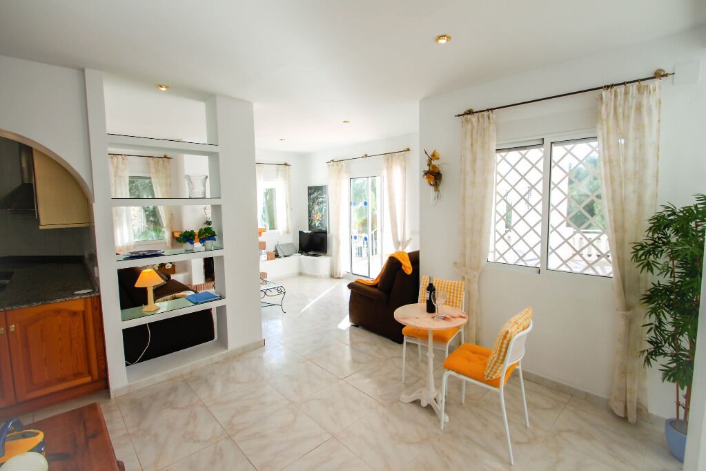 A spacious living area with a kitchen, a dining table with chairs, and a large window with curtains.