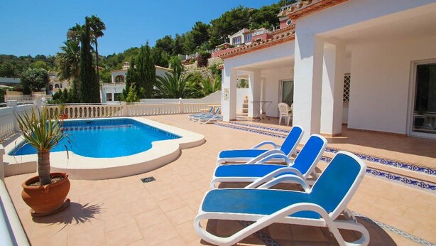 A pool area with lounge chairs, a palm tree, and a view of the surrounding landscape. - Sesam - sea view villa with private pool in Moraira (Teulada)