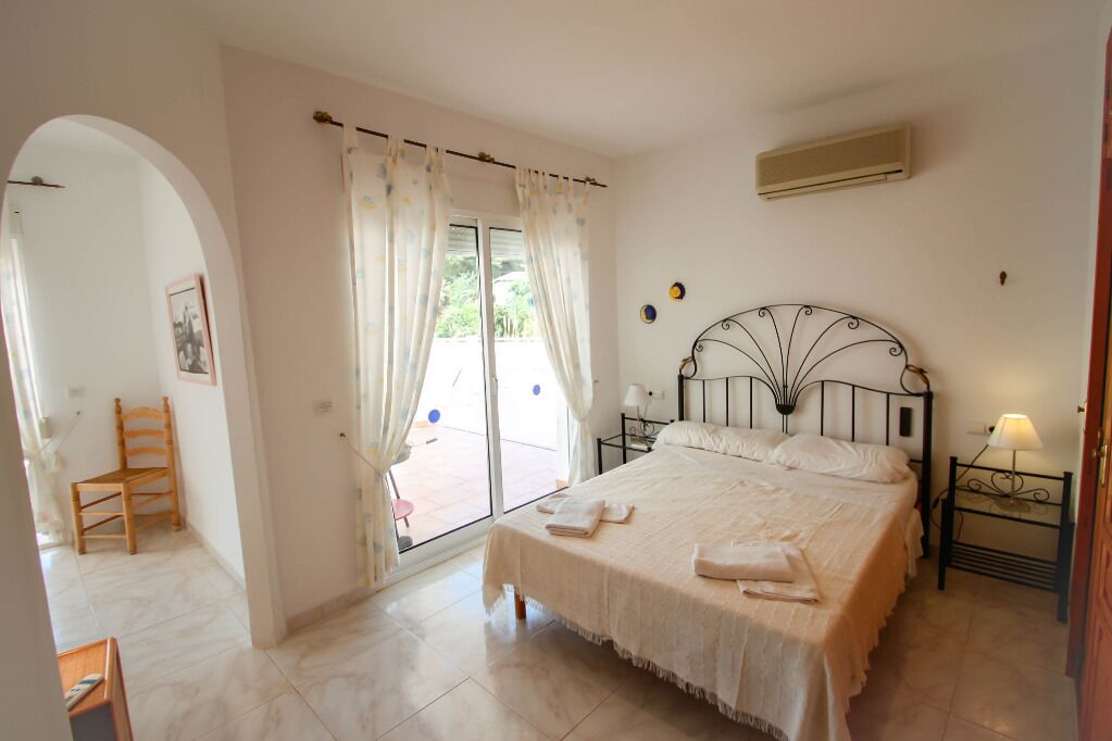 A bedroom with a bed, a chair, a nightstand, and a window with curtains.