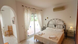 A bedroom with a bed, a chair, a nightstand, and a window with curtains. - Sesam - sea view villa with private pool in Moraira (Teulada)