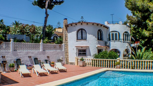 Zona de piscina amb gandules, un mur de pedra i una piscina.