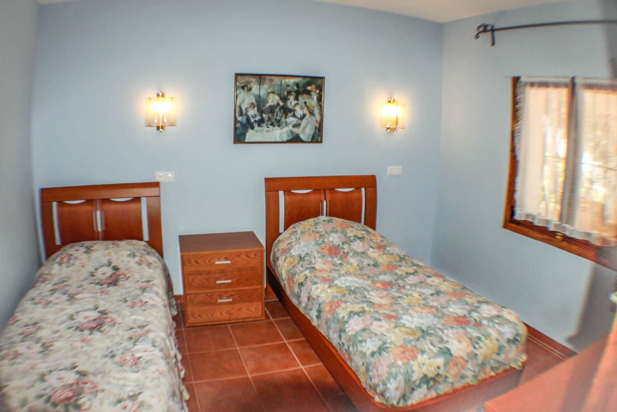 A bedroom with two single beds, a nightstand, a painting on the wall, and two wall-mounted lights.