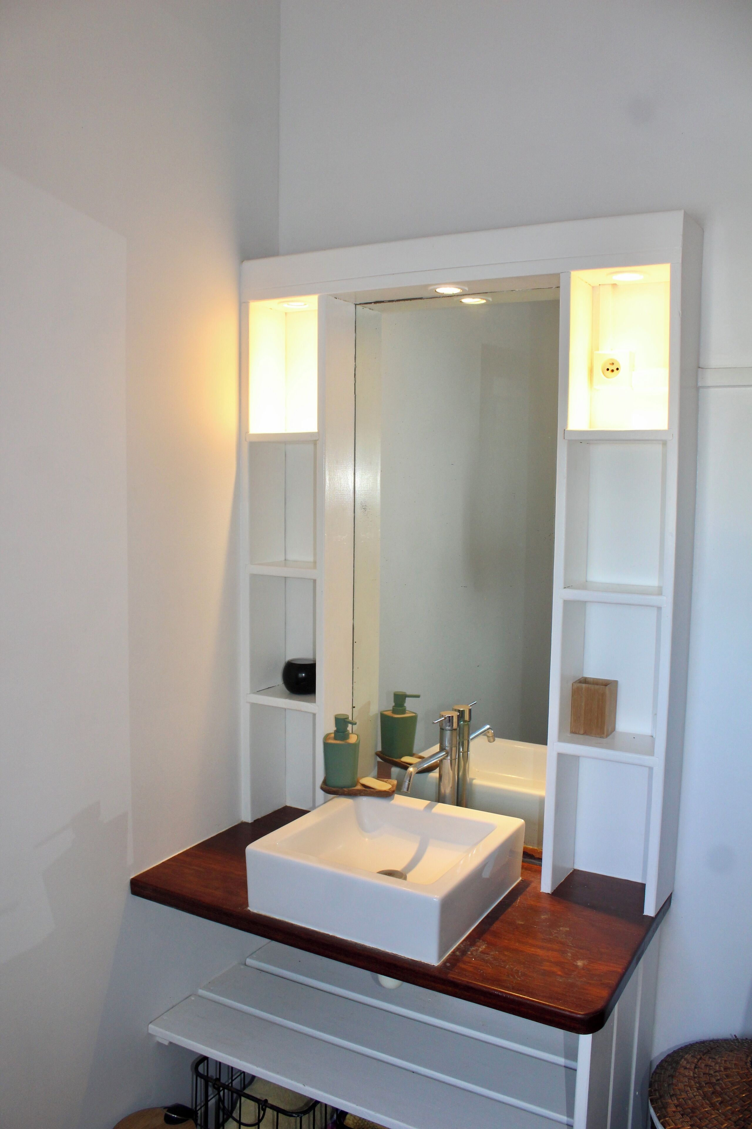 Een badkamer met een witte wastafel, een spiegel en planken met toiletartikelen.