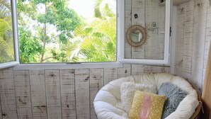 Une pièce dotée d’une grande fenêtre, d’un fauteuil en osier blanc agrémenté de coussins et d’un mur en bois.