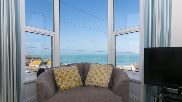 Sala de estar con un ventanal que ofrece vista al mar y un sillón con cojines estampados.
