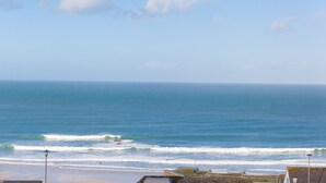 Vista costera con olas, cielo despejado y una línea de costa distante.