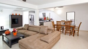 A modern living room with a sectional sofa, a dining area with wooden chairs, a kitchen with a refrigerator and stove, and a ceiling fan. - Le Bougainvillier, magnificent villa with breathtaking views (Oyster Pond)