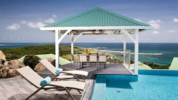 A pool area with lounge chairs and a gazebo overlooking a coastal view.