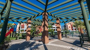 Un espace extérieur abrité, doté d’une structure en colonnes de briques, d’une aire de jeux avec un toboggan et d’un chemin pavé.