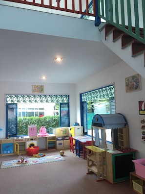 Una sala de juegos infantil con una cocinita, juguetes y una casita.