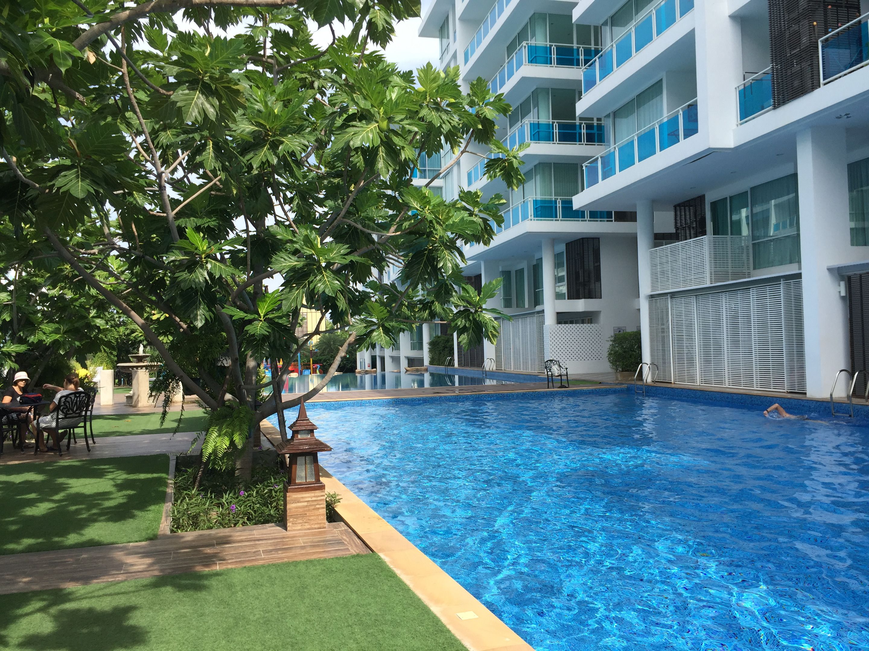A modern hotel with a swimming pool, outdoor seating, and a well-maintained garden.