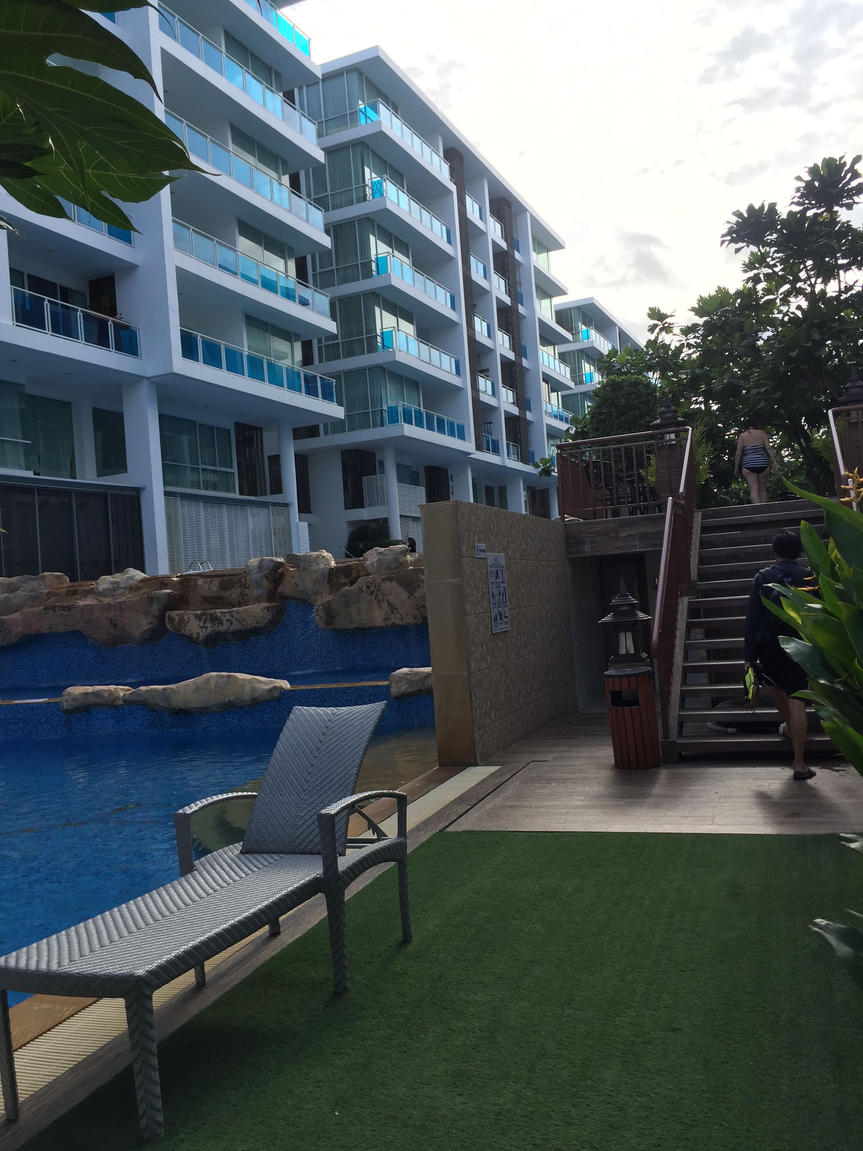 A modern hotel with a swimming pool, outdoor seating, and a staircase leading to the upper floors.