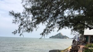 Paredes de pedra com uma estátua de uma figura sentada, um deck de madeira com assentos e vista para o mar e uma ilha ao longe.