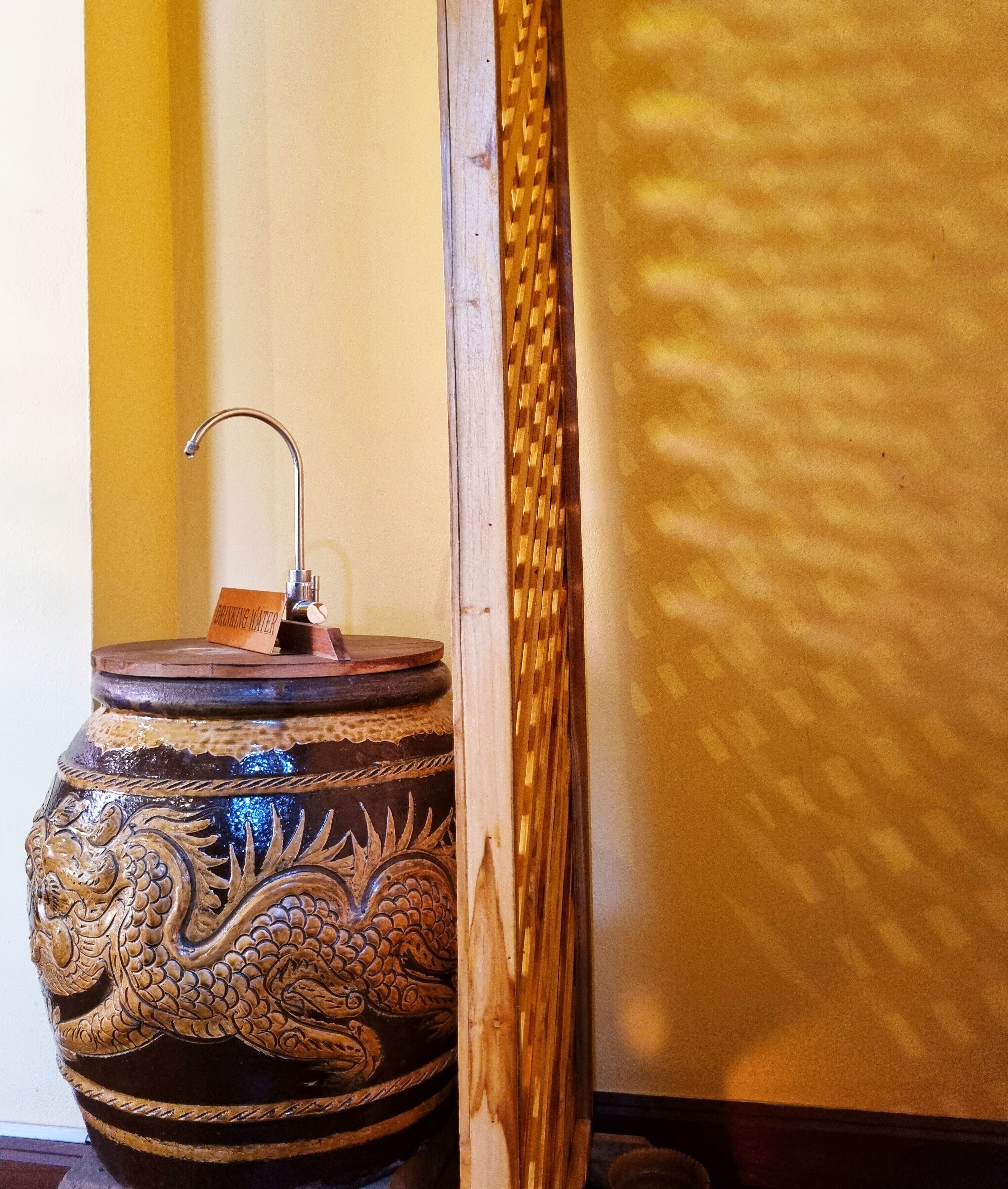 A decorative ceramic pot with a dragon design and a faucet, placed against a wall with a woven texture.