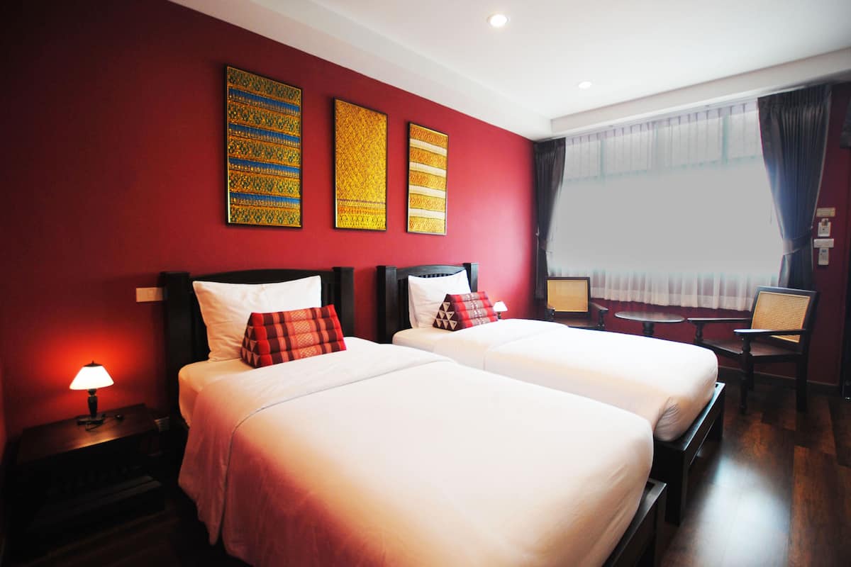 A hotel room with two beds, a small table, a chair, and artwork on the wall.