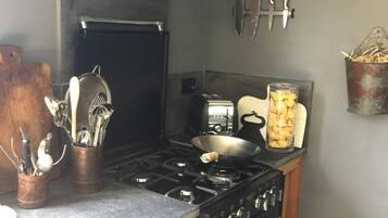 A compact kitchen with a gas stove, oven, and a black range hood. There are utensils in a wooden holder, a toaster, and a jar of cookies on the counter.