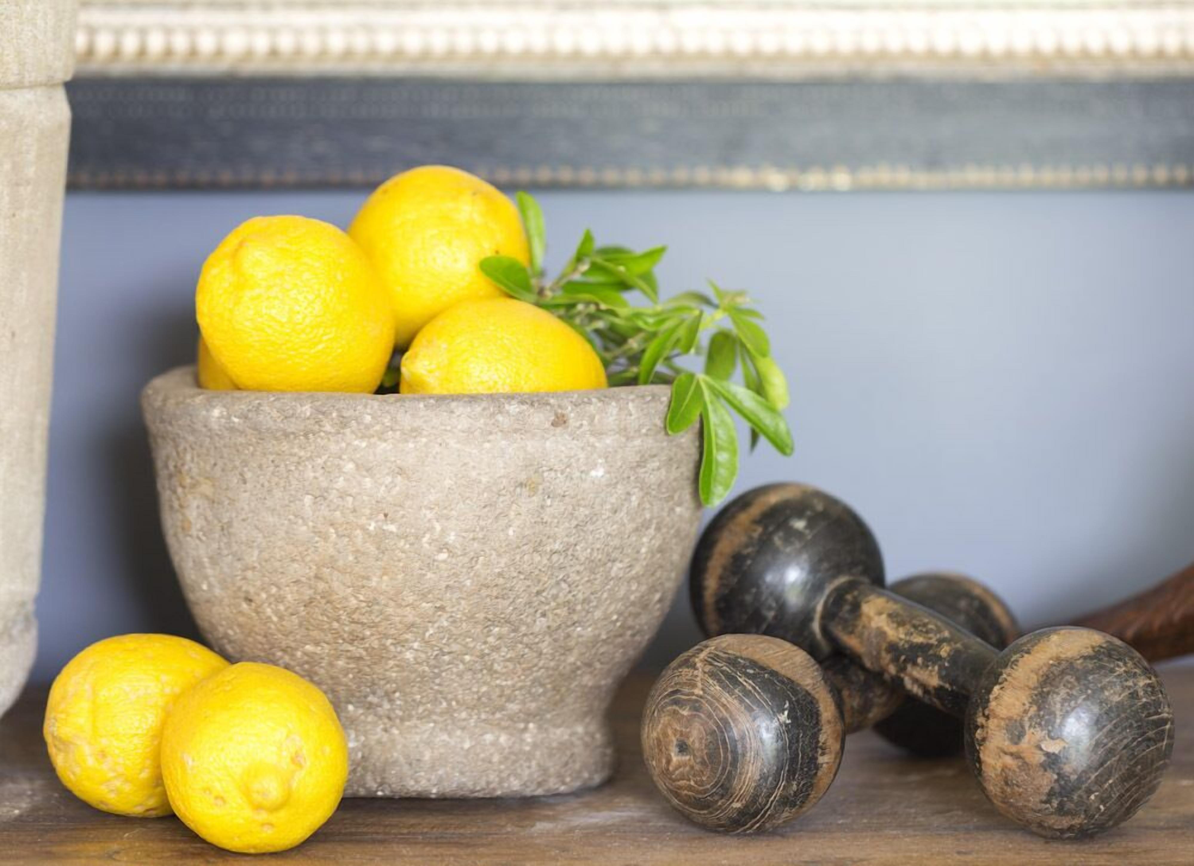 Un mortero de piedra con limones y una ramita de romero.