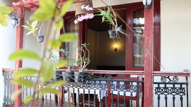 A balcony with wrought iron railings, potted plants, and hanging flower baskets. - Nhi Trung Hotel (Da Nang)