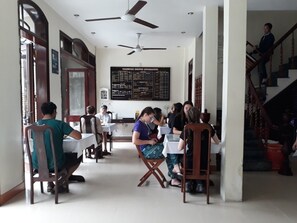 A restaurant with tables and chairs, a menu board, and a staircase. - Nhi Trung Hotel (Da Nang)