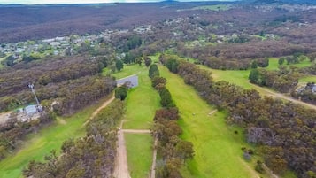Une vue aérienne d’un paysage rural avec un terrain de golf, entouré de forêts denses et d’un petit groupe de bâtiments.