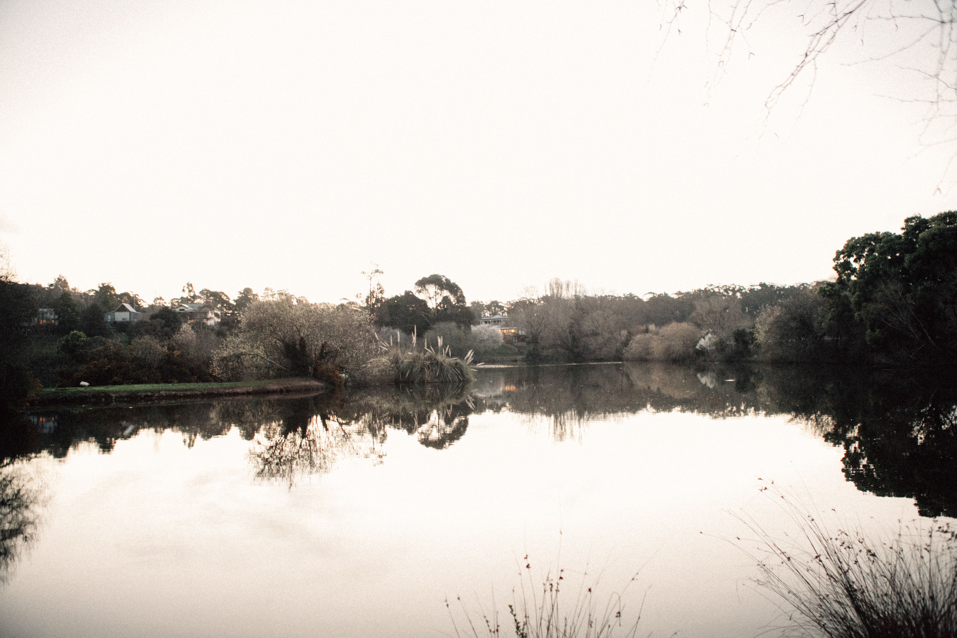 A calm lake with reflections of trees and a distant building.