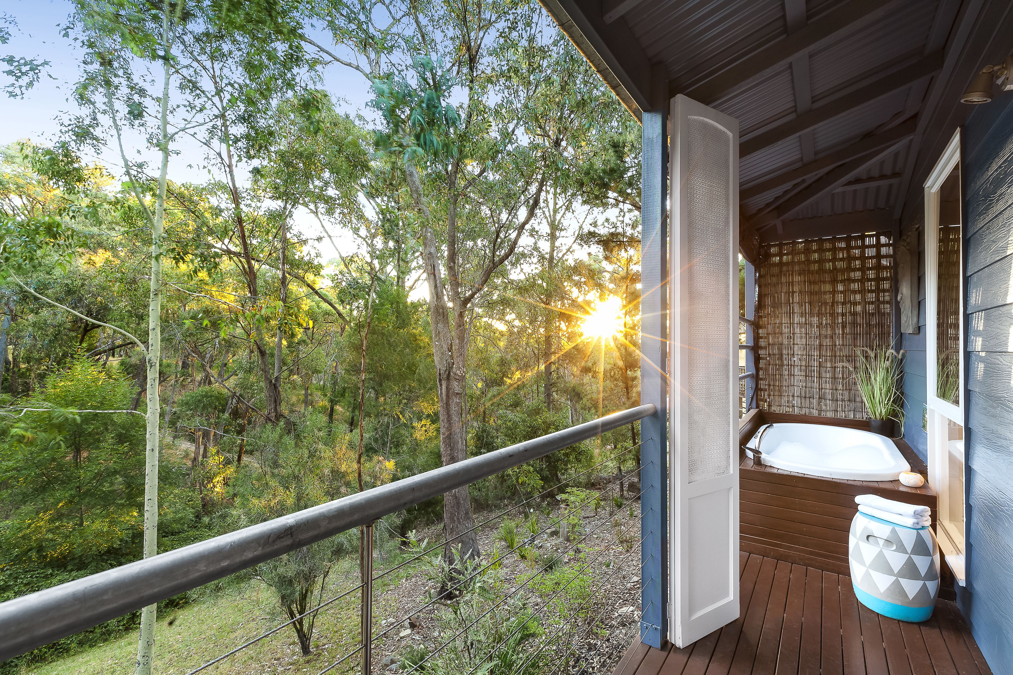 A wooden deck with a glass balustrade overlooking a forested area, a hot tub, and a bamboo screen.
