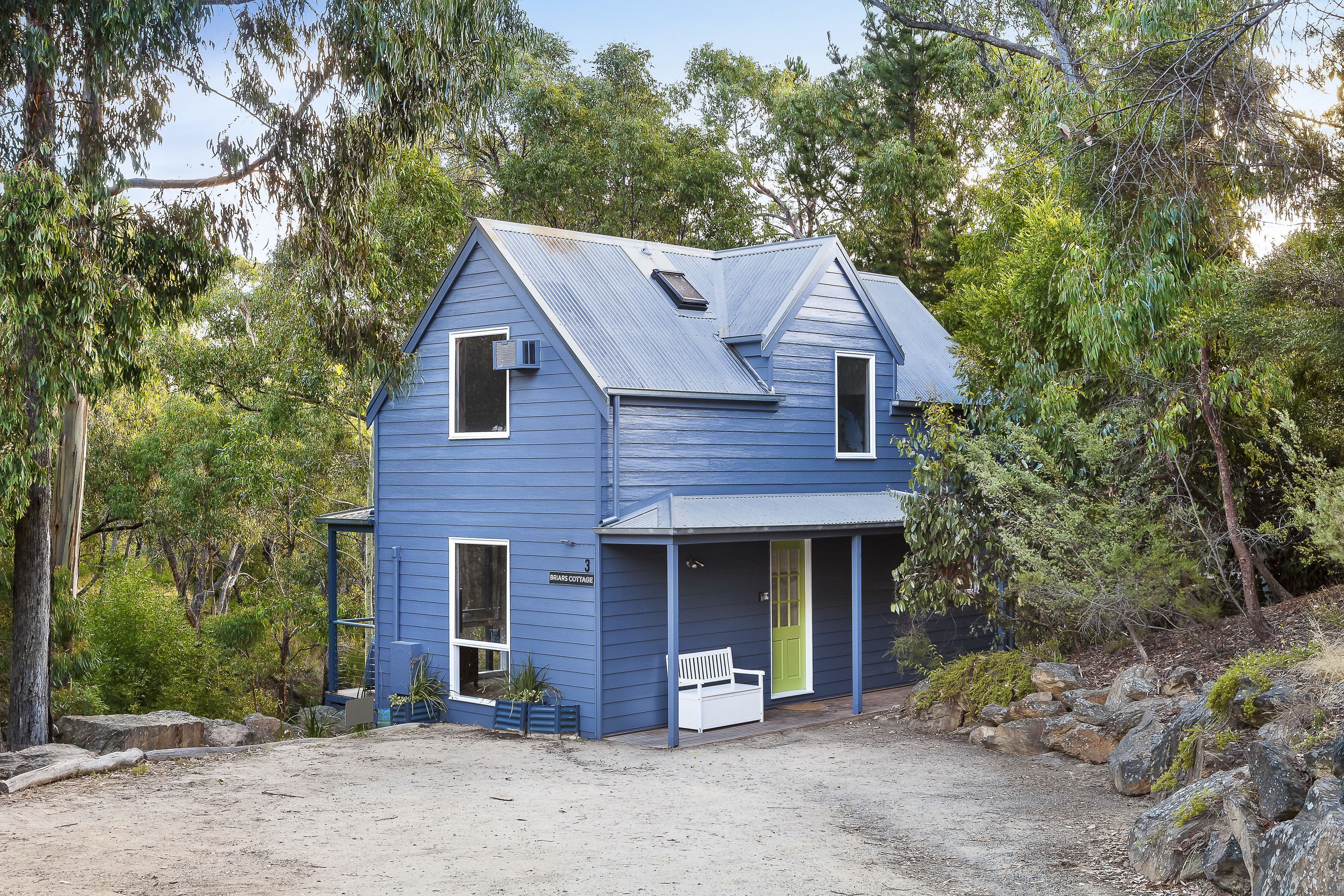 A two-story blue house with a porch, a green door, and a small bench.