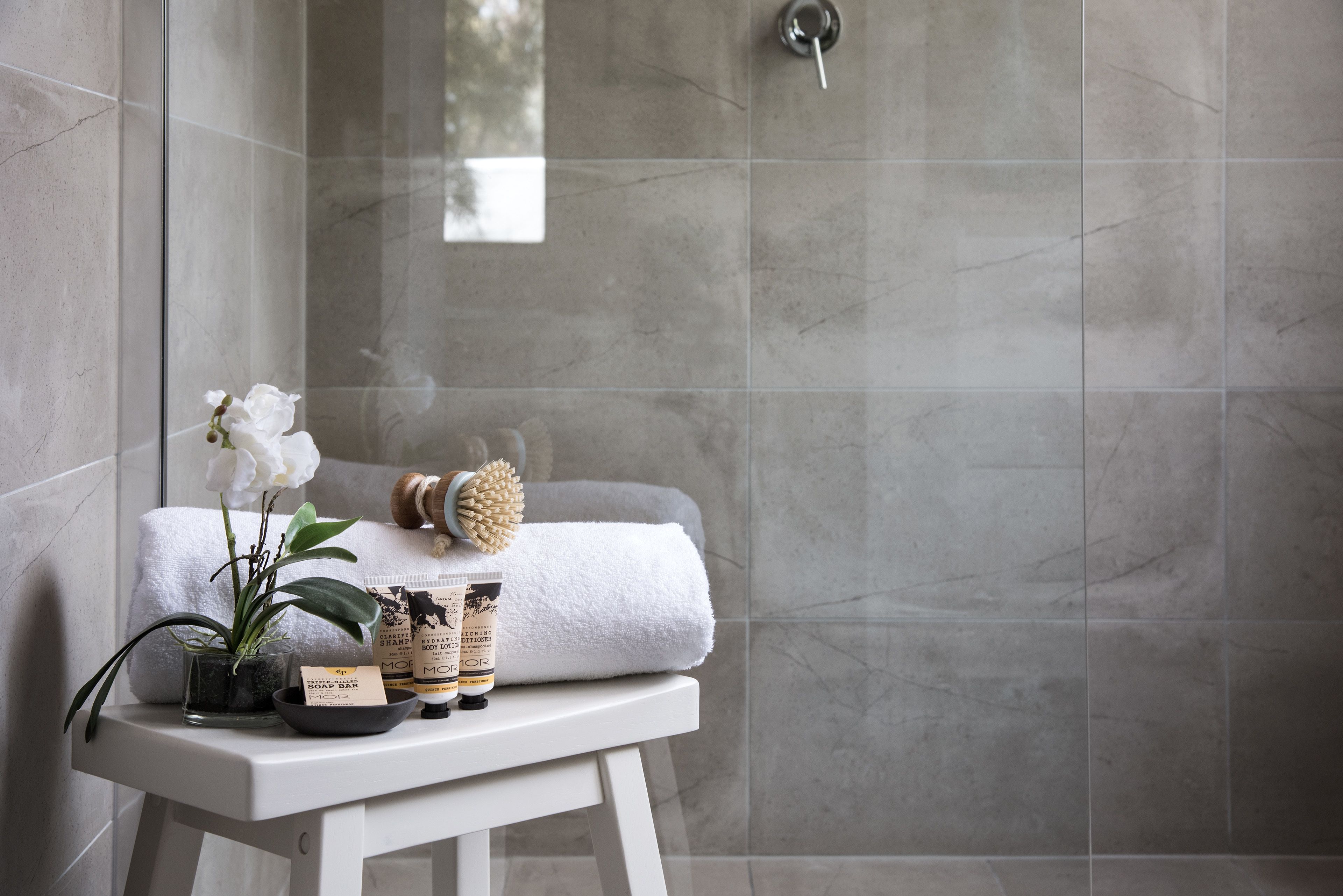A bathroom with a white bench, a white towel, a hairbrush, and a potted orchid.