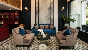 A modern living room with a blue sofa, two armchairs, and a coffee table. There is a red bar area with shelves and decorative items. - Golden Rooster Hotel (Hanoi)