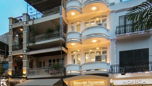 A multi-story building with balconies, a restaurant named "Golden Rooster" on the ground floor, and a store named "Monica" on the right. - Golden Rooster Hotel (Hanoi)