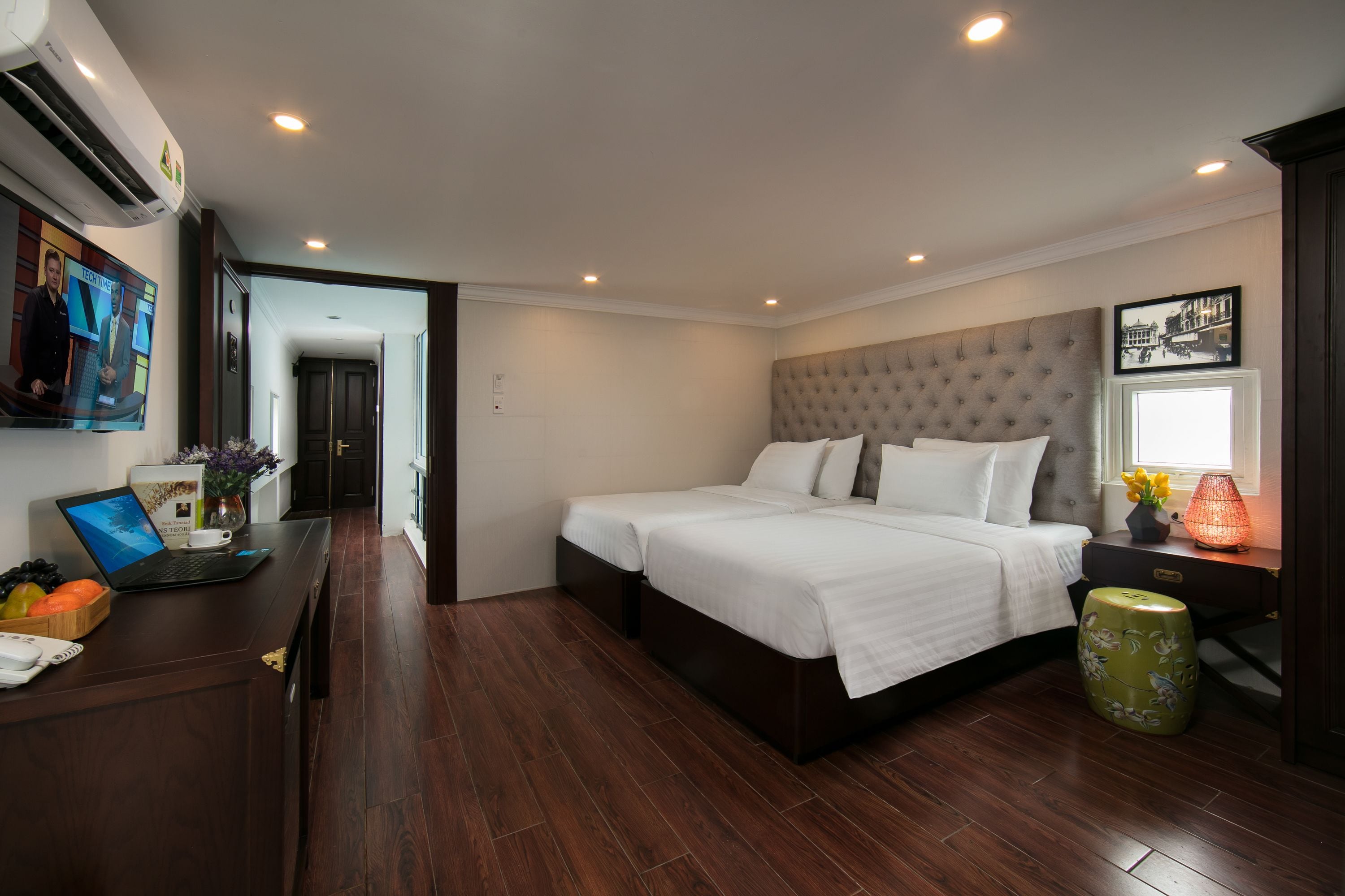 A modern hotel room with a large bed, a desk with a laptop, and a small stool.