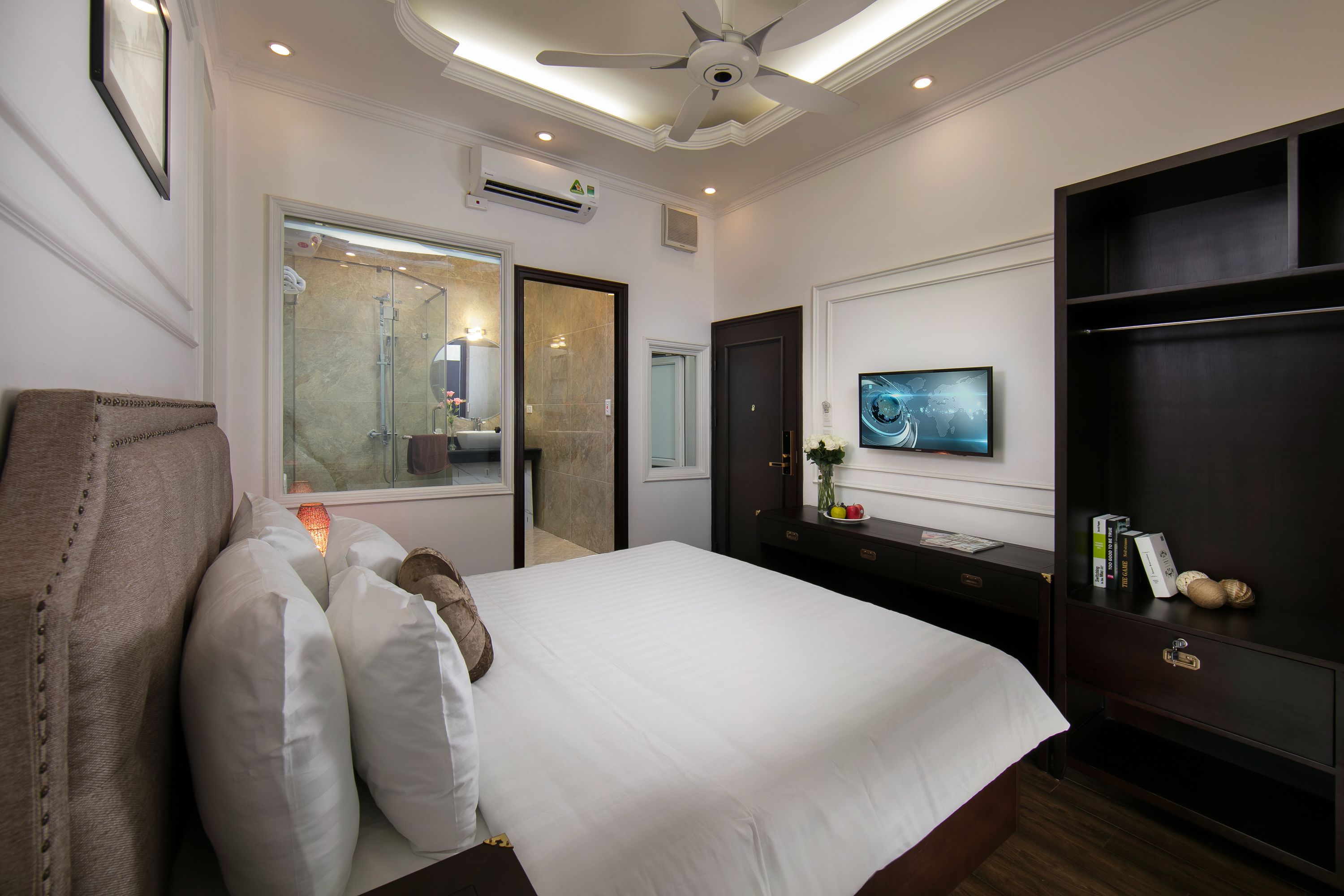 Une chambre d’hôtel avec un grand lit, un téléviseur à écran plat, une armoire et un ventilateur de plafond.