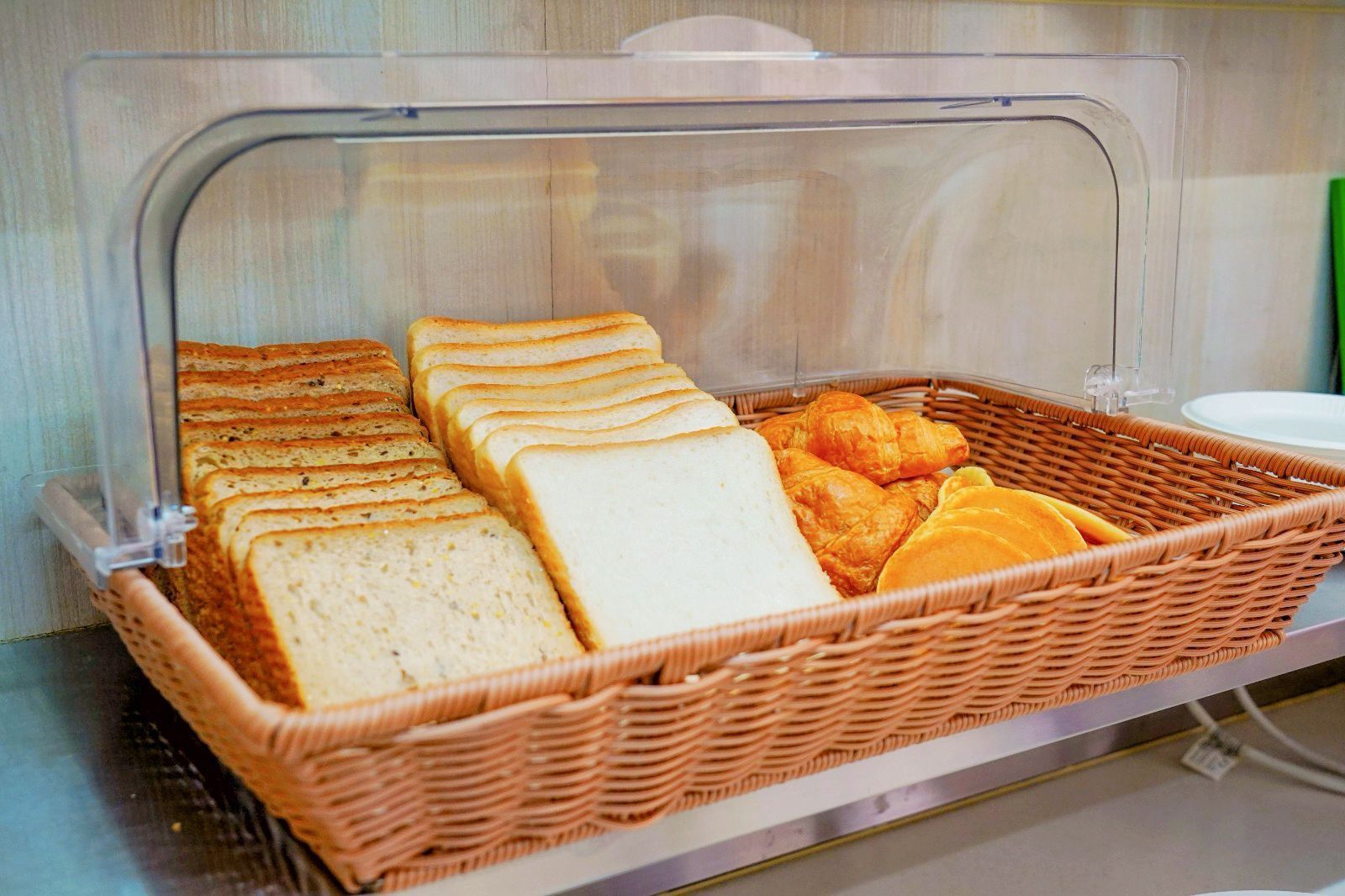 A breakfast buffet with sliced bread, croissants, and orange slices in a wicker basket.