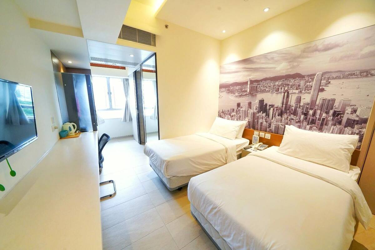 A hotel room with two beds, a TV, a desk, and a cityscape view.
