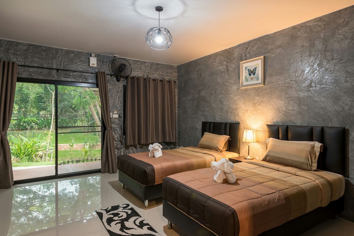 A hotel room with two beds, a large window with curtains, a ceiling fan, and a wall-mounted light fixture.