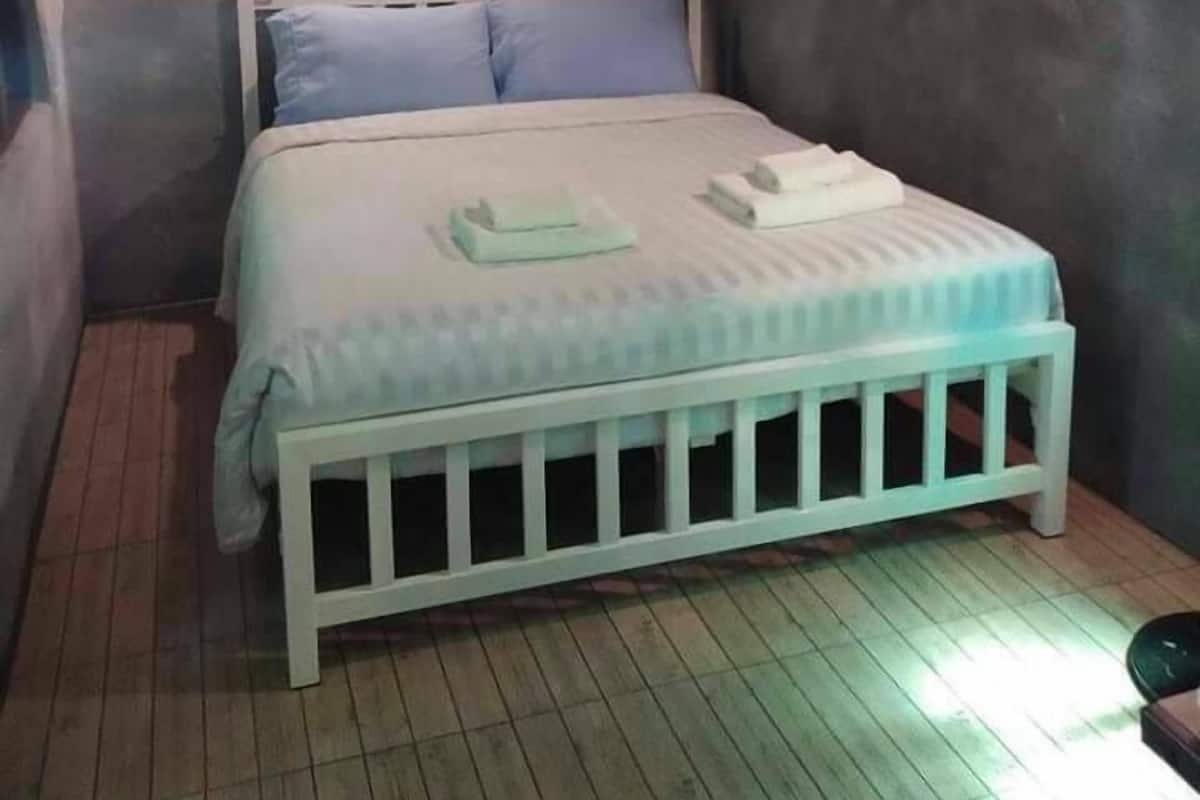 A small, dimly lit room with a single bed, a white crib, and a wall-mounted air conditioner.