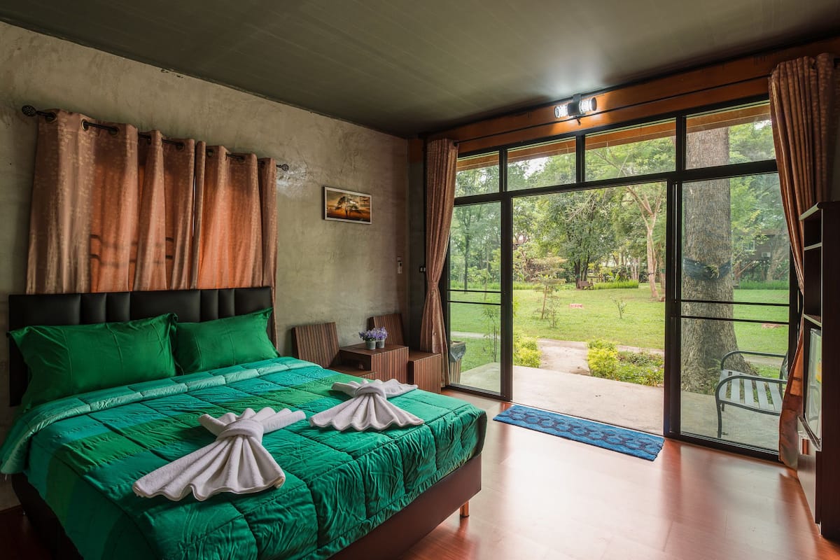 A bedroom with a large bed, a view of the outdoors, and a wooden headboard.