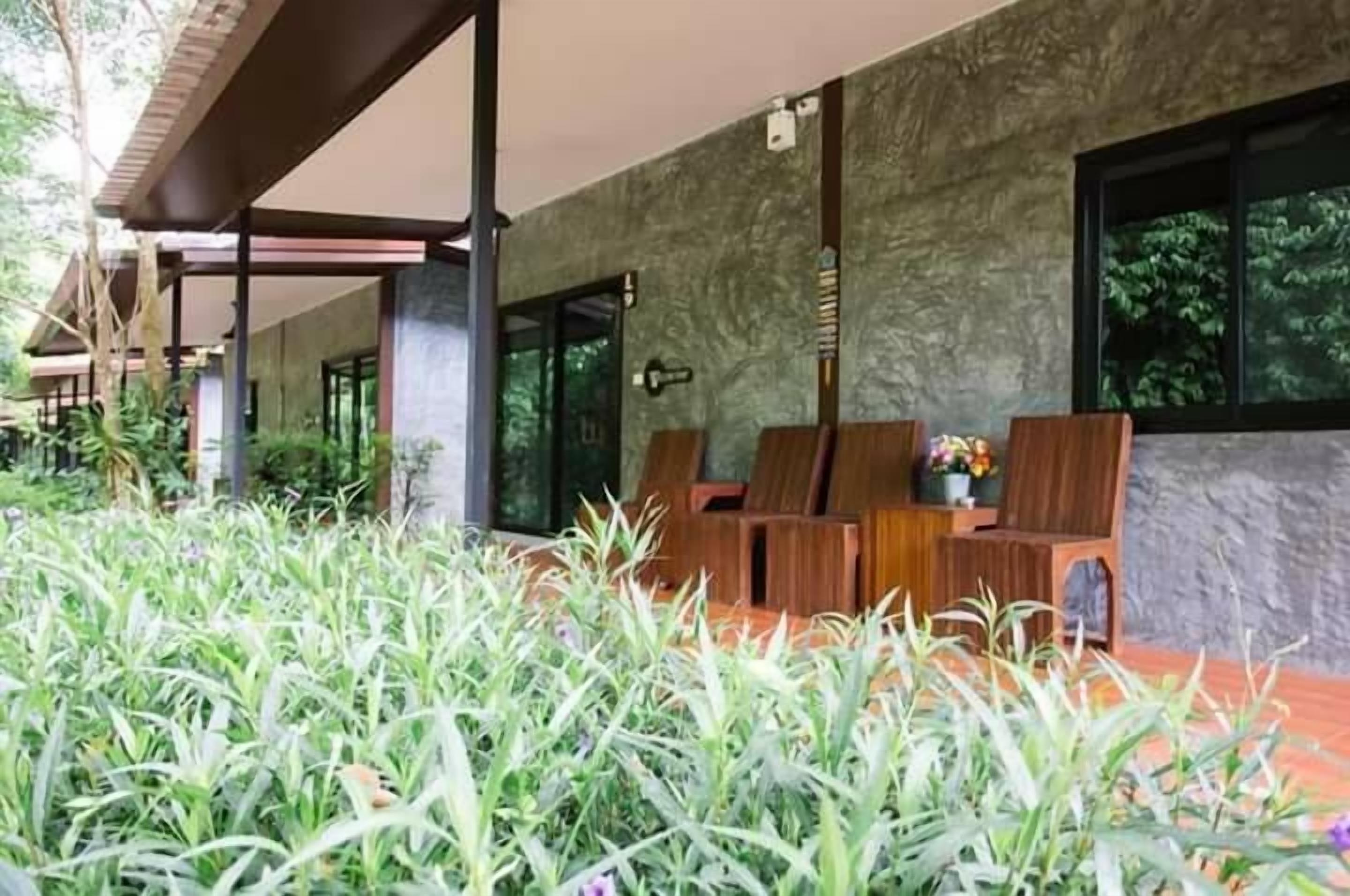 Un edificio moderno con una zona salotto esterna coperta, pareti in pietra e vegetazione rigogliosa.