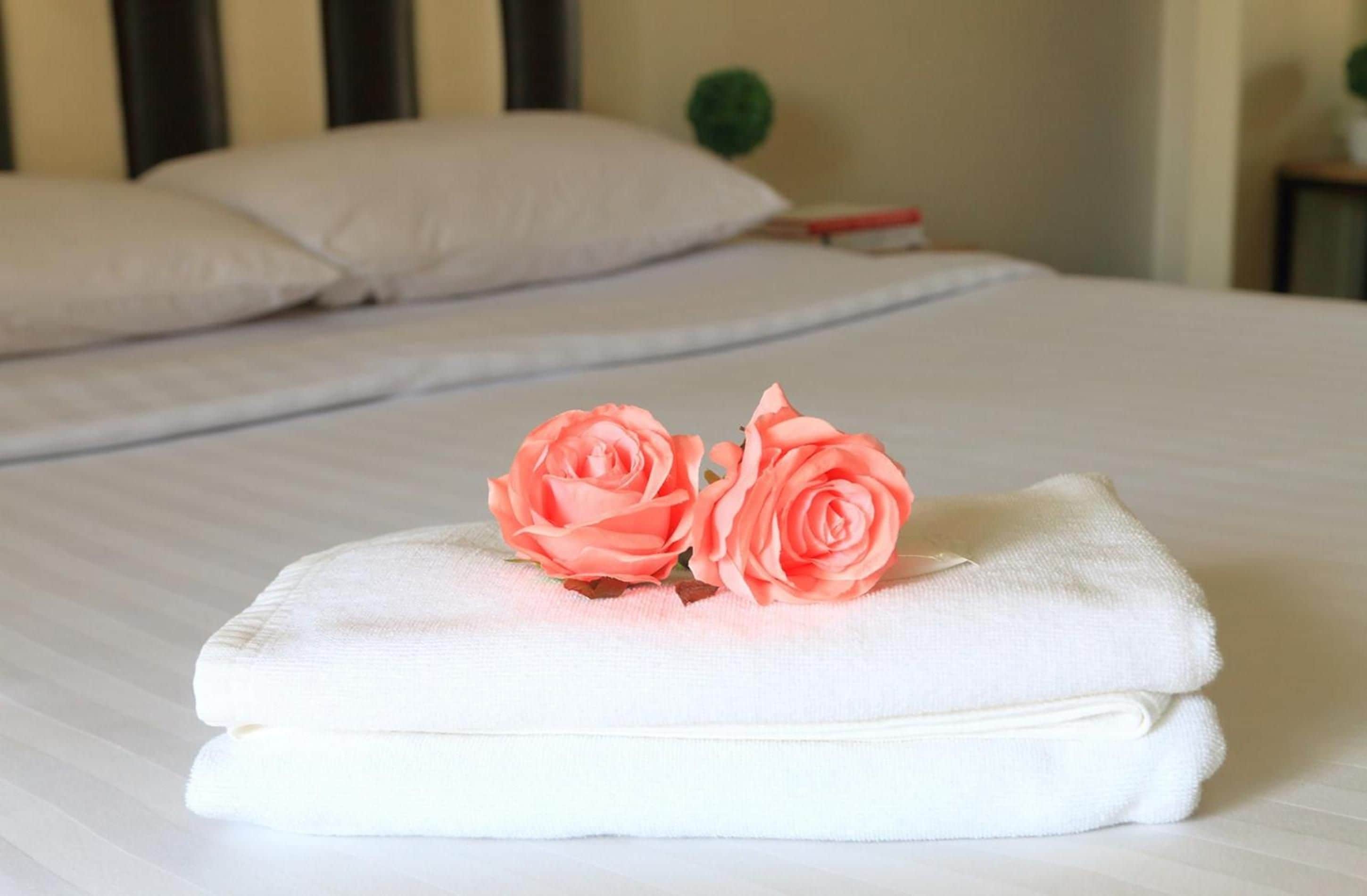 Una cama bien hecha con dos toallas dobladas y dos rosas rosas encima.