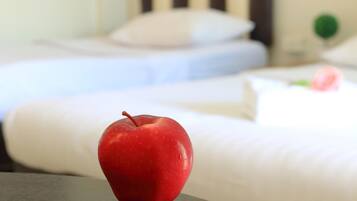 A red apple on a table in a hotel room with white bedding and a green object in the background.