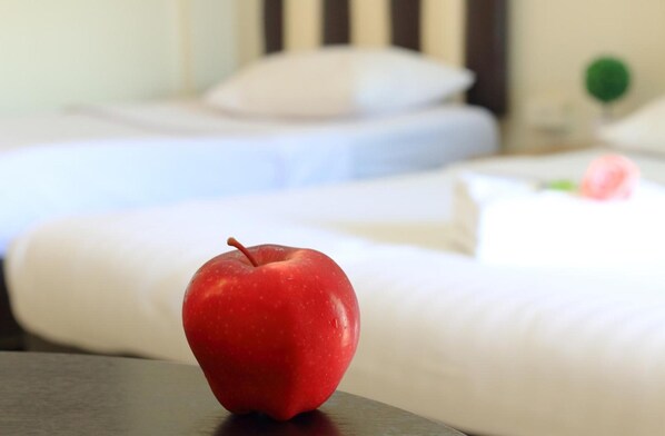 A red apple on a table in a hotel room with white bedding and a green object in the background.