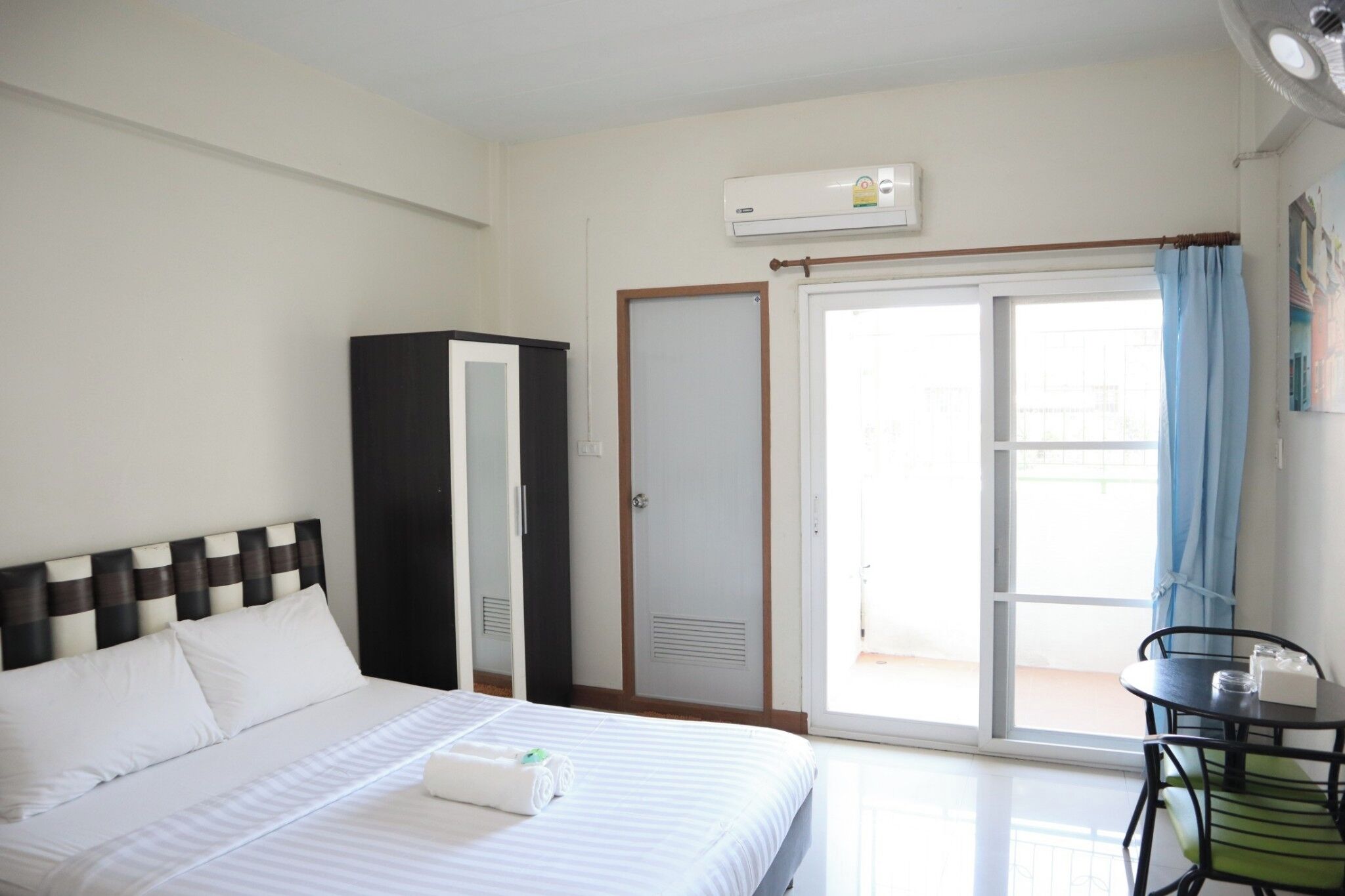 A hotel room with a bed, a wardrobe, a desk, and a sliding glass door to the balcony.