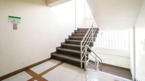 A staircase with metal railings, white walls, and a window with a grid pattern. - SK Resort (Bangkok)