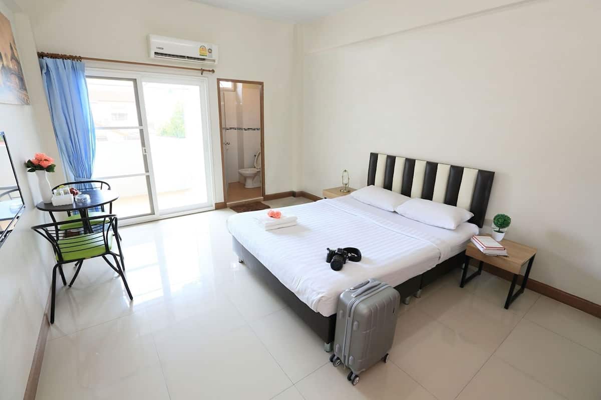 A hotel room with a bed, a desk, a chair, a suitcase, and a small table with a plant.