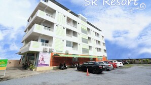 A multi-story hotel with balconies, a parking area, and a clear sky. - SK Resort (Bangkok)