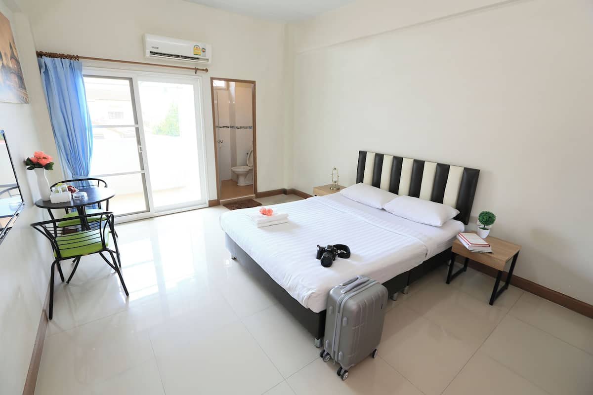 A hotel room with a bed, a suitcase, a small table with a book, a chair, and a view of the bathroom through an open door.