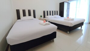 Two neatly made beds with white linens and dark headboards, a small bedside table with a book and a plant, and a wardrobe in the background. - SK Resort (Bangkok)