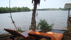 A lakeside setting with wooden lounge chairs and a small table, surrounded by greenery and a palm tree. - Mahi Villa (Bentota)